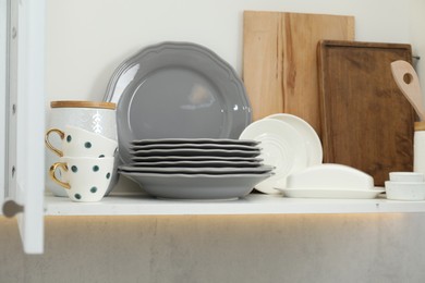 Photo of Clean dishware and cups on shelf in cabinet indoors