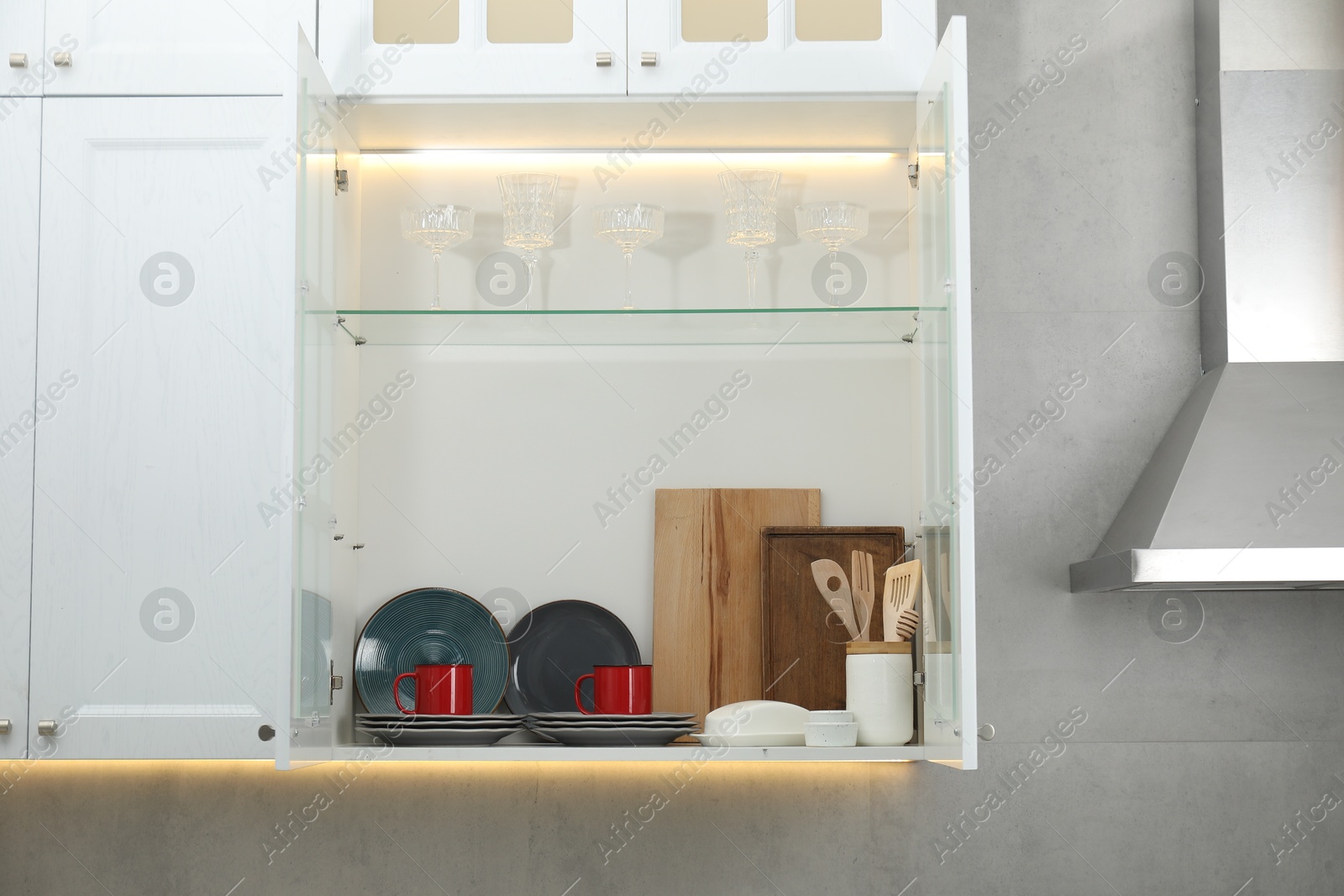Photo of Clean dishware and glasses on shelves in cabinet indoors