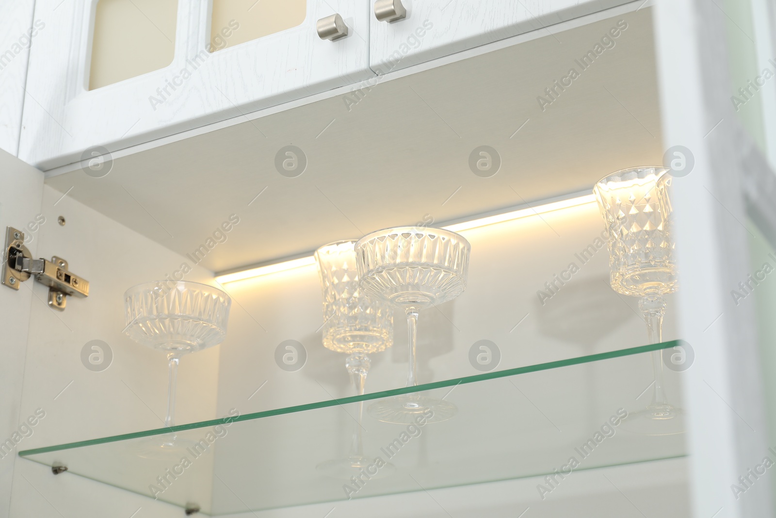 Photo of Clean glasses on shelf in cabinet indoors, low angle view