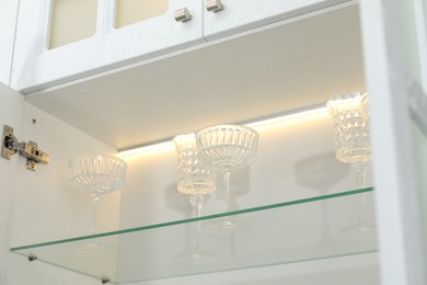 Photo of Clean glasses on shelf in cabinet indoors, low angle view