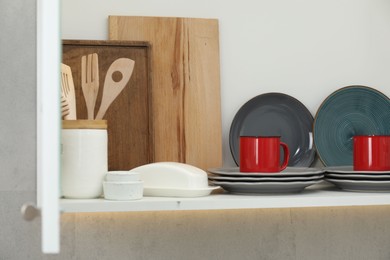 Photo of Clean dishware and cups on shelf in cabinet indoors