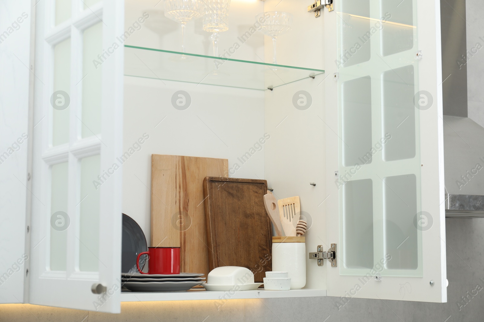 Photo of Clean dishware and glasses on shelves in cabinet indoors