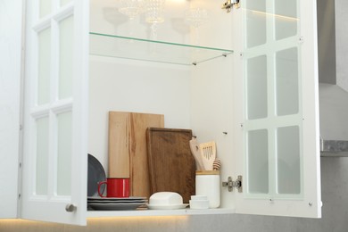Photo of Clean dishware and glasses on shelves in cabinet indoors