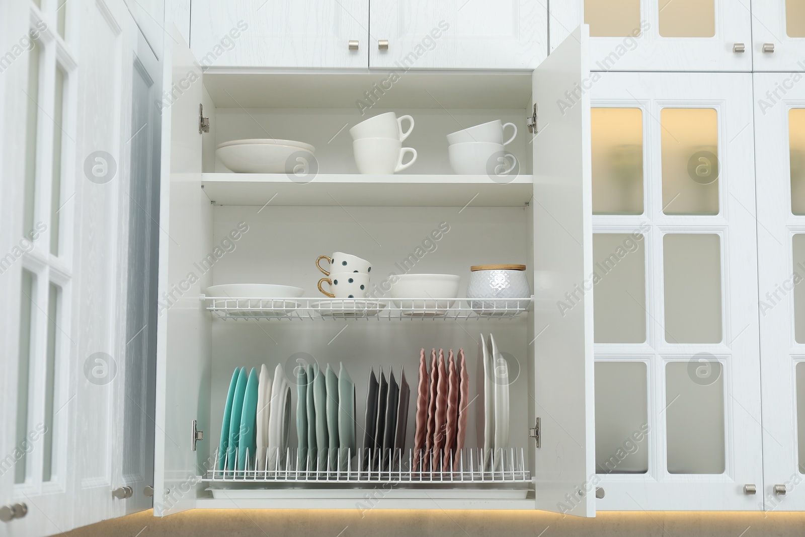 Photo of Clean dishware and cups on shelves in cabinet indoors