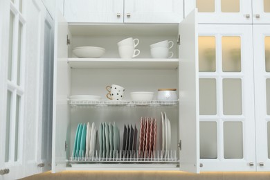 Photo of Clean dishware and cups on shelves in cabinet indoors