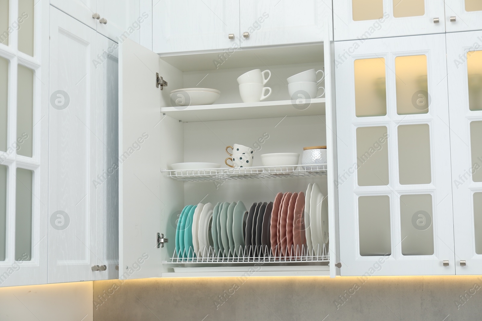 Photo of Clean dishware and cups on shelves in cabinet indoors