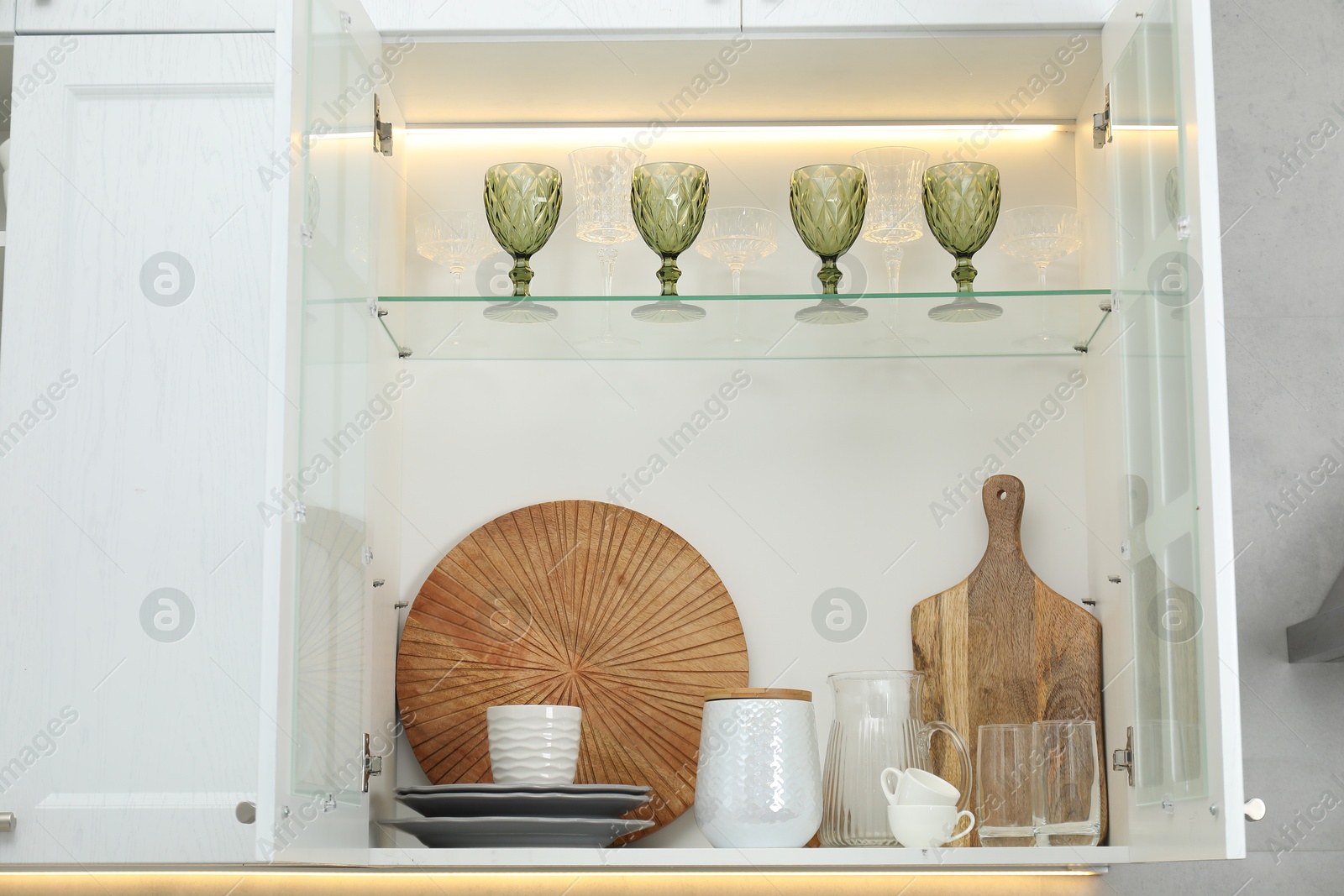 Photo of Clean dishware and glasses on shelves in cabinet indoors