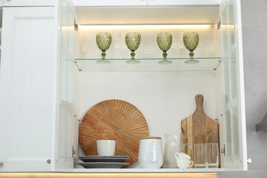 Photo of Clean dishware and glasses on shelves in cabinet indoors