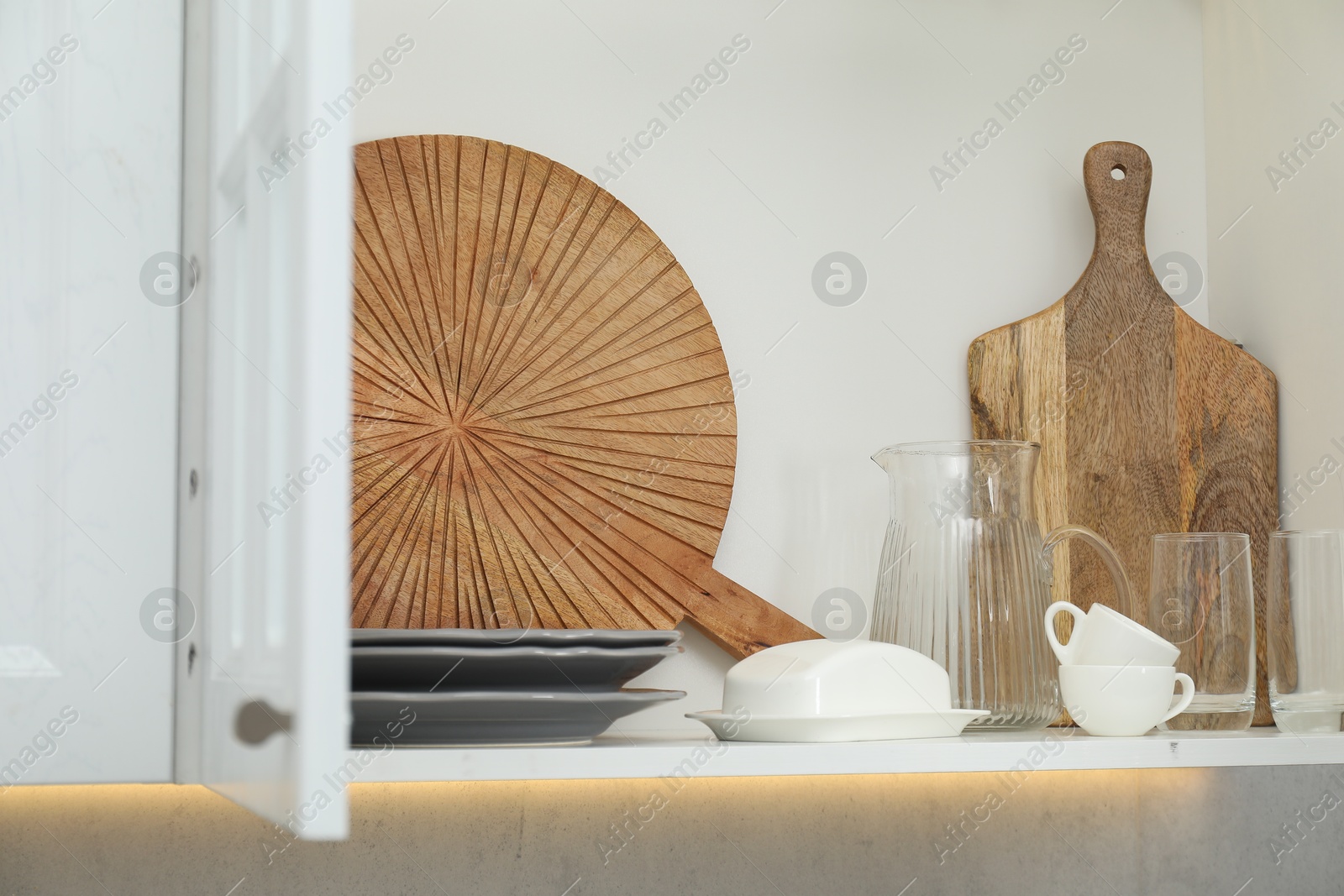 Photo of Clean dishware and cups on shelf in cabinet indoors
