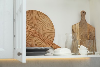 Photo of Clean dishware and cups on shelf in cabinet indoors