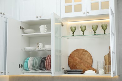Photo of Clean dishware, cups and glasses on shelves in cabinets indoors