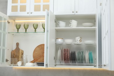 Photo of Clean dishware, cups and glasses on shelves in cabinets indoors