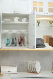 Photo of Clean dishware, cups and glasses on shelves in cabinets indoors