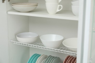 Photo of Clean dishware and cups on shelves in cabinet indoors