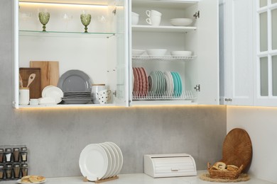 Photo of Clean dishware, cups and glasses on shelves in cabinets indoors
