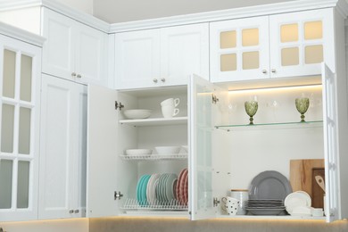 Photo of Clean dishware, cups and glasses on shelves in cabinets indoors