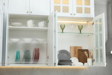 Photo of Clean dishware, cups and glasses on shelves in cabinets indoors