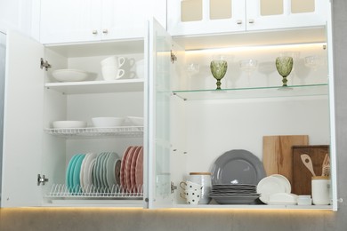 Photo of Clean dishware, cups and glasses on shelves in cabinets indoors