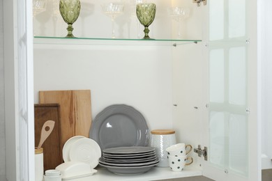 Photo of Clean dishware, cups and glasses on shelves in cabinet indoors