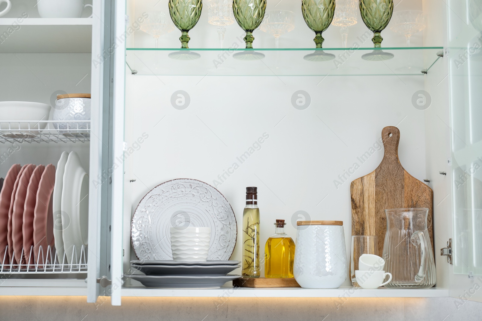 Different dishware, glasses and other kitchen utensils on shelves in cabinets indoors Photo of Different dishware, glasses and other kitchen utensils on shelves in cabinets indoors