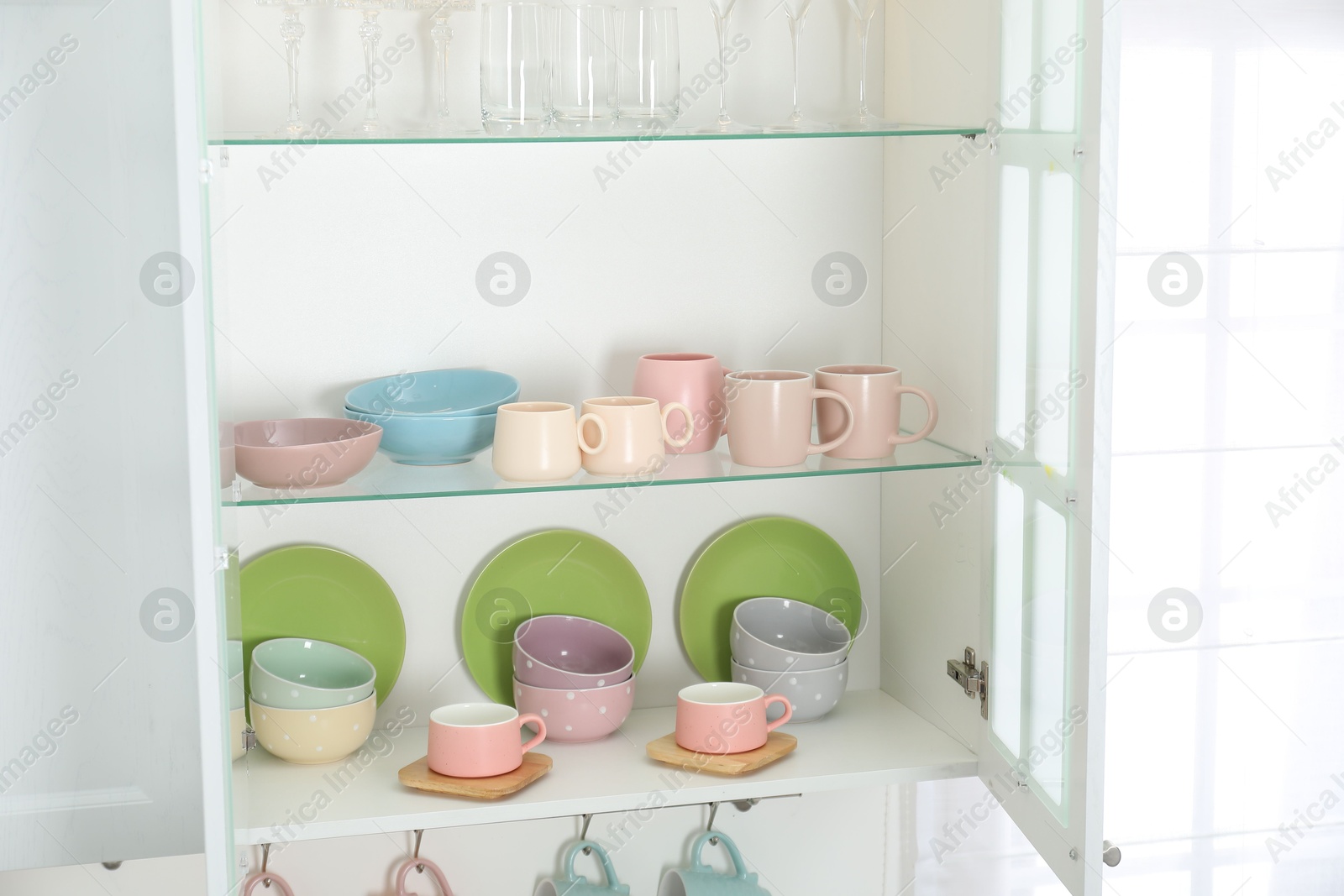 Photo of Different dishware, glasses and cups on shelves in cabinet indoors