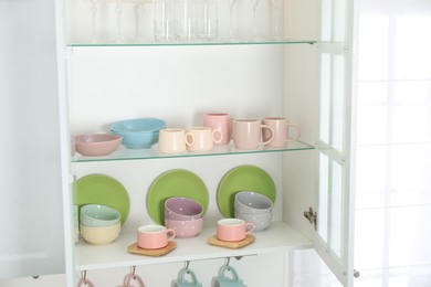 Photo of Different dishware, glasses and cups on shelves in cabinet indoors