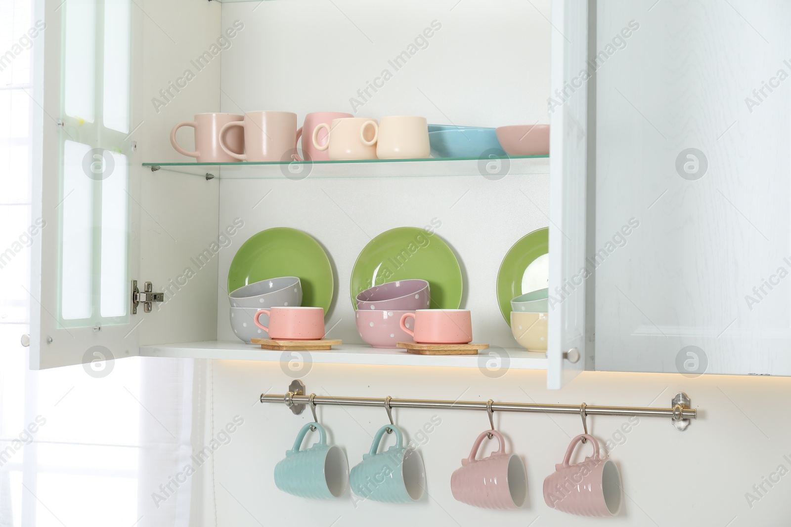 Photo of Different dishware and cups on shelves in cabinet indoors