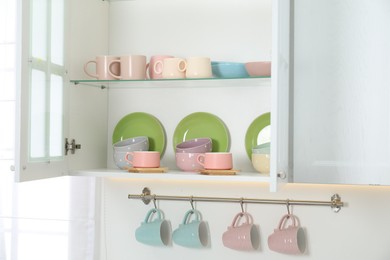 Photo of Different dishware and cups on shelves in cabinet indoors