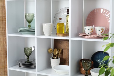 Photo of Shelving unit with different dishware, glasses and other kitchen utensils indoors