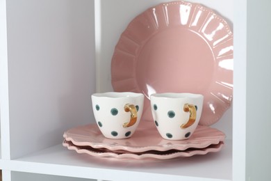 Photo of Clean plates and cups on shelf indoors, closeup