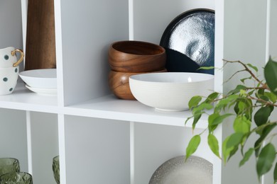 Photo of Different clean dishware and cups on shelves indoors, closeup