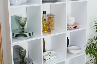 Photo of Shelving unit with different dishware, glasses, spices and pasta indoors