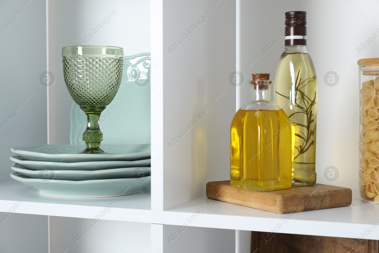 Photo of Clean plates, glass, spices and pasta on shelves indoors, closeup