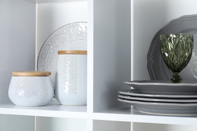 Photo of Clean dishware and glass on shelves indoors, closeup
