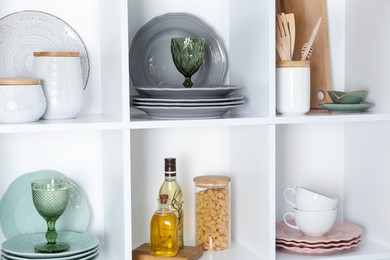 Photo of Shelving unit with different dishware, glasses and other kitchen utensils indoors