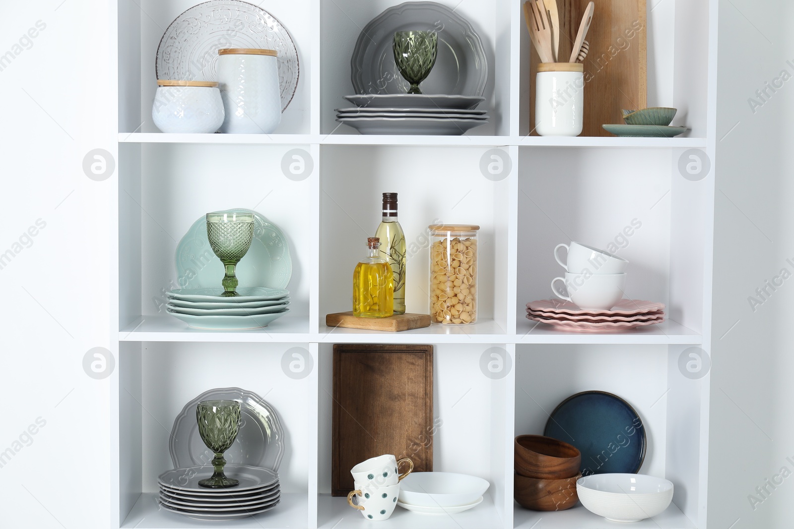 Photo of Shelving unit with different dishware, glasses and other kitchen utensils near white wall indoors