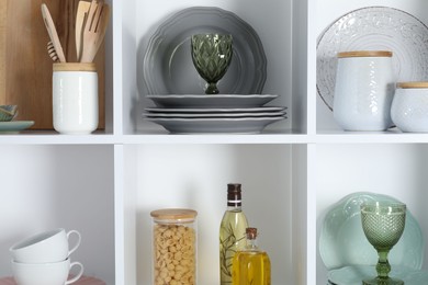 Photo of Shelving unit with different dishware, glasses and other kitchen utensils indoors