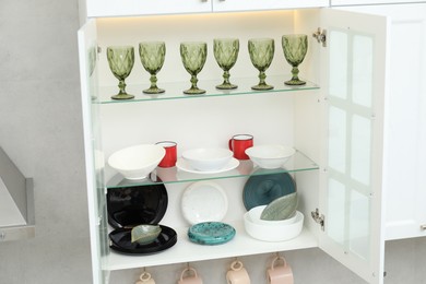 Photo of Clean dishware, cups and glasses on shelves in cabinet indoors