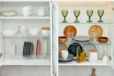 Photo of Clean dishware, cups and glasses on shelves in cabinets indoors