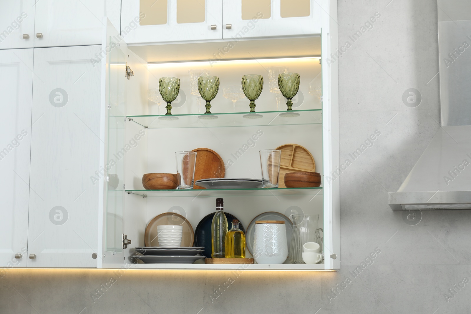 Different dishware, glasses and other kitchen utensils on shelves in cabinet indoors Photo of Different dishware, glasses and other kitchen utensils on shelves in cabinet indoors