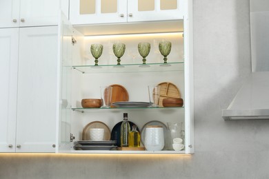 Photo of Different dishware, glasses and other kitchen utensils on shelves in cabinet indoors