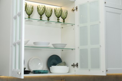 Photo of Different dishware and glasses on shelves in cabinet indoors