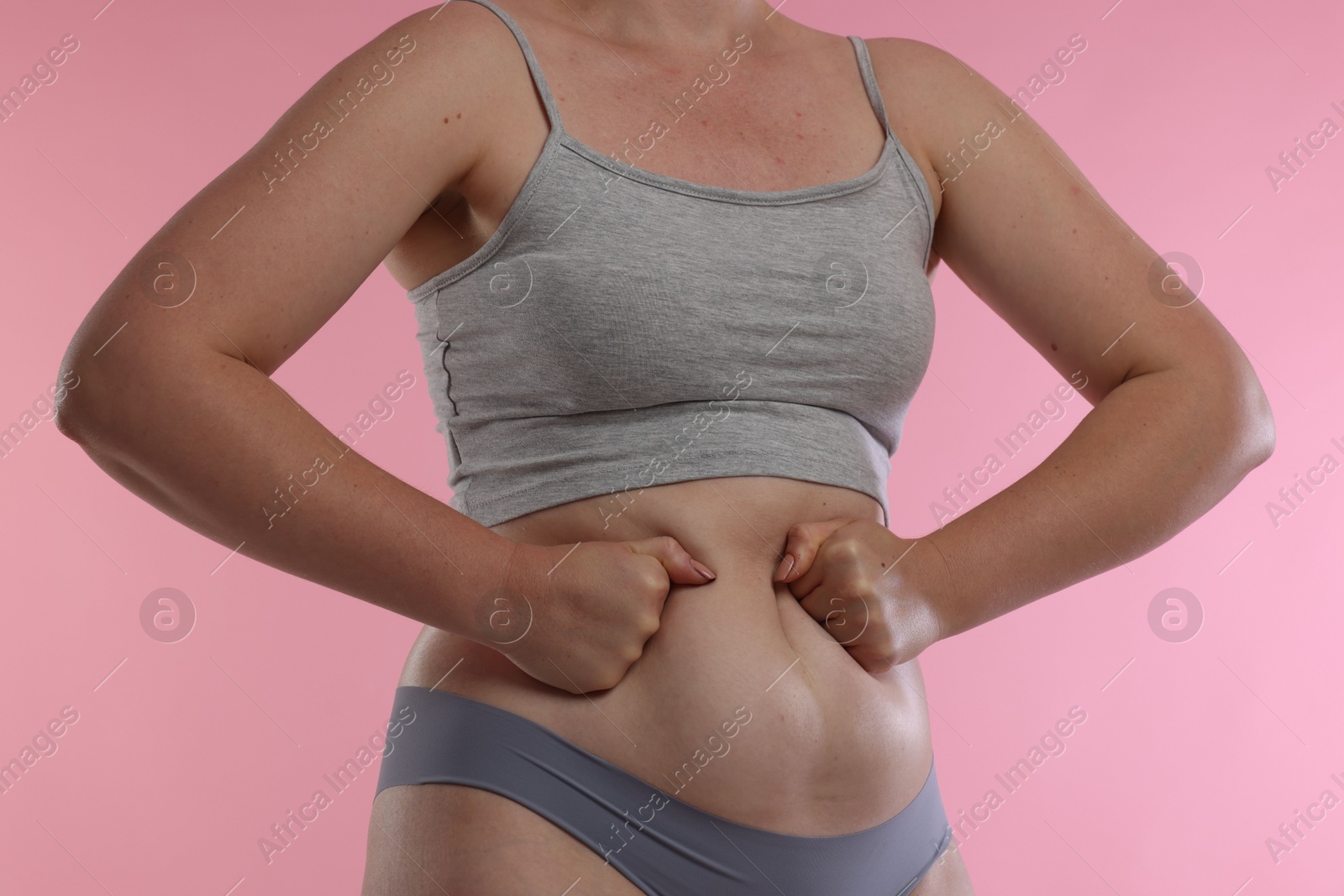 Photo of Liposuction. Woman in underwear touching her belly on pink background, closeup
