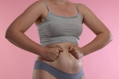 Photo of Liposuction. Woman in underwear touching her belly on pink background, closeup