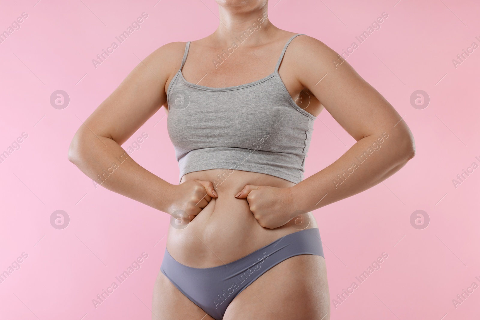 Photo of Liposuction. Woman in underwear touching her belly on pink background, closeup