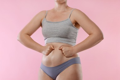 Photo of Liposuction. Woman in underwear touching her belly on pink background, closeup