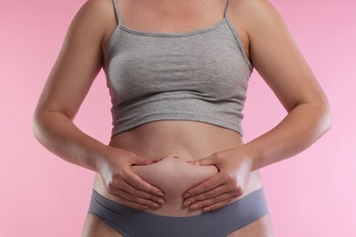 Photo of Liposuction. Woman in underwear touching her belly on pink background, closeup