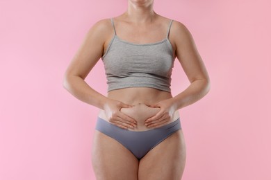 Photo of Liposuction. Woman in underwear touching her belly on pink background, closeup