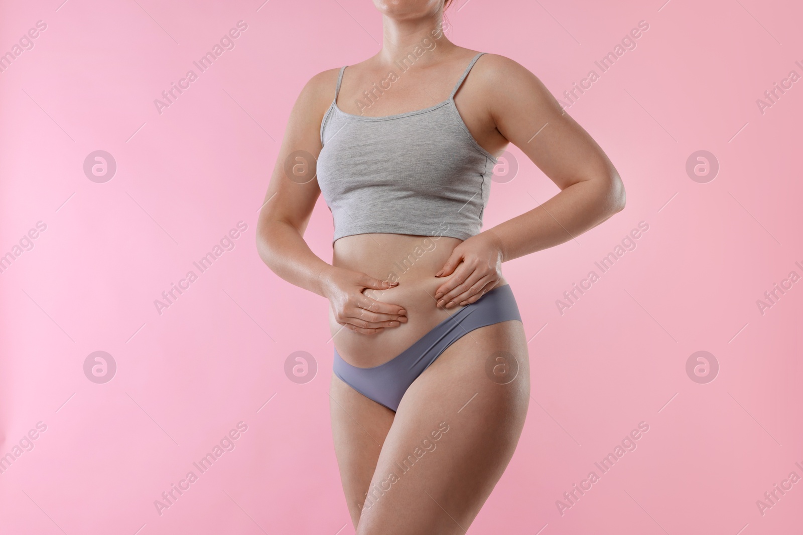 Photo of Liposuction. Woman in underwear touching her belly on pink background, closeup