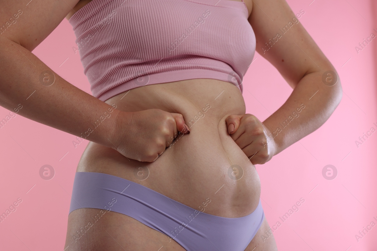 Photo of Liposuction. Woman in underwear touching her belly on pink background, closeup